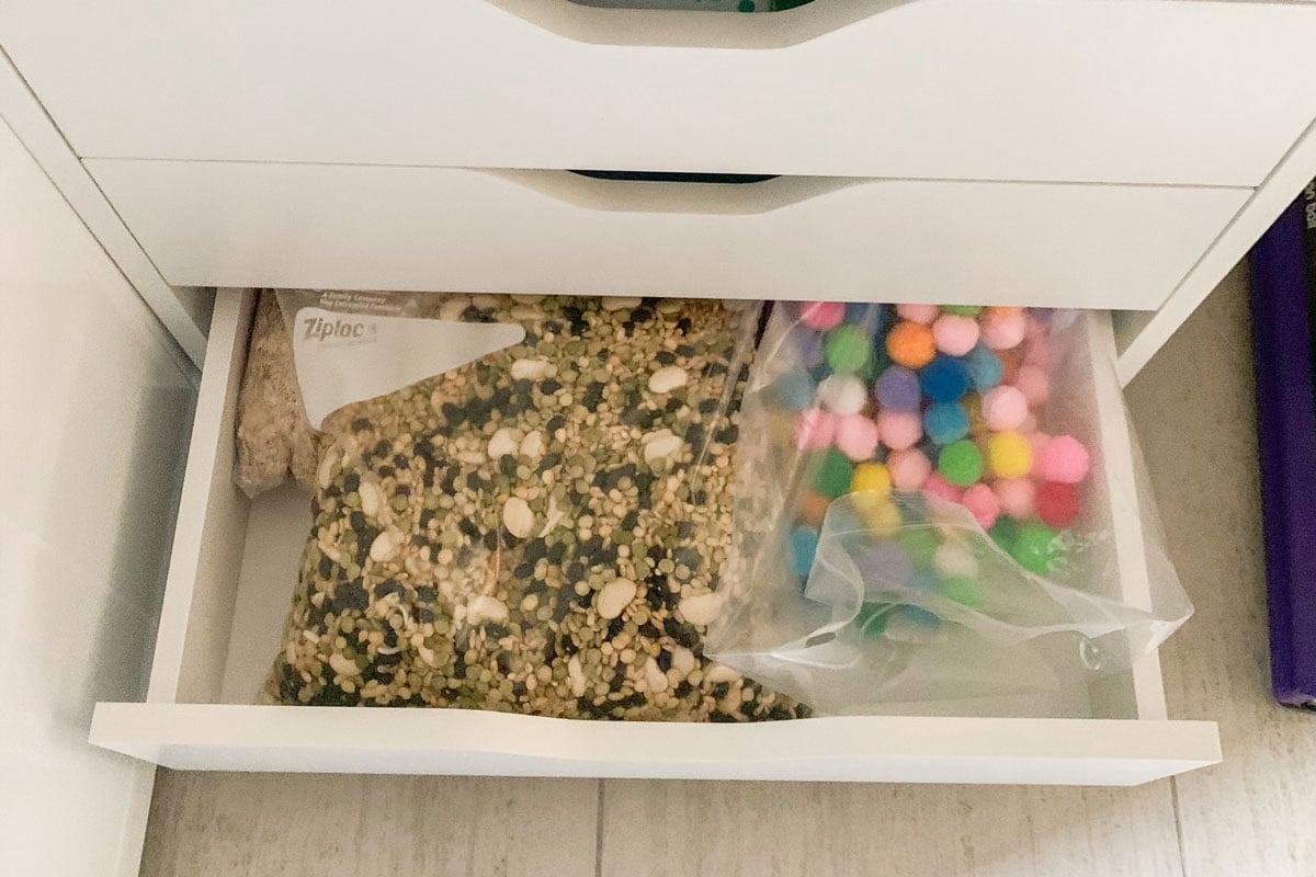 A white drawer is open showing a back of mixed dried beans, dry oats, and pom pom balls.