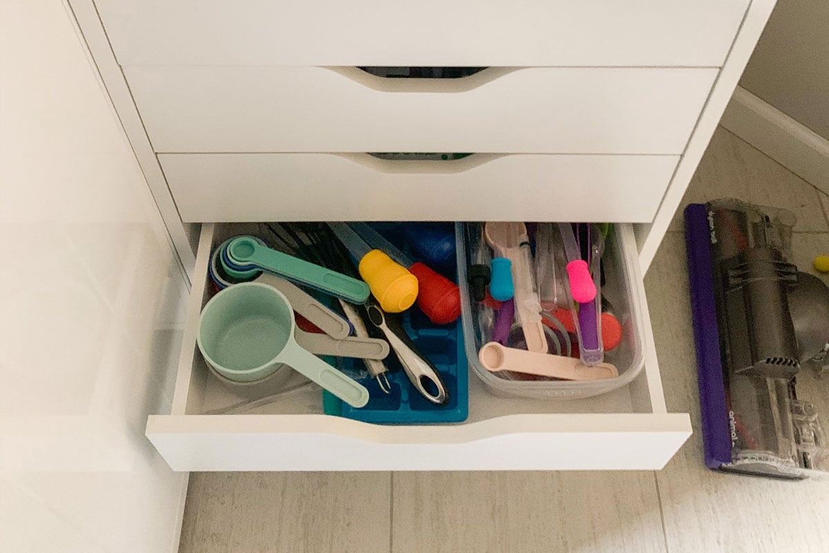 A drawer is open to show sensory bin tools for children: measuring cups, liquid droppers, ice cube tray, and plastic tongs.
