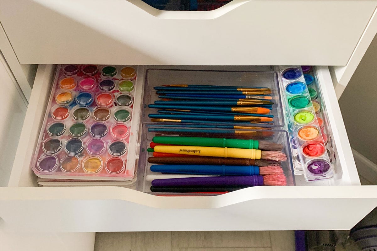 A white drawer is open to show two sets of watercolors and different sizes of paint brushes.