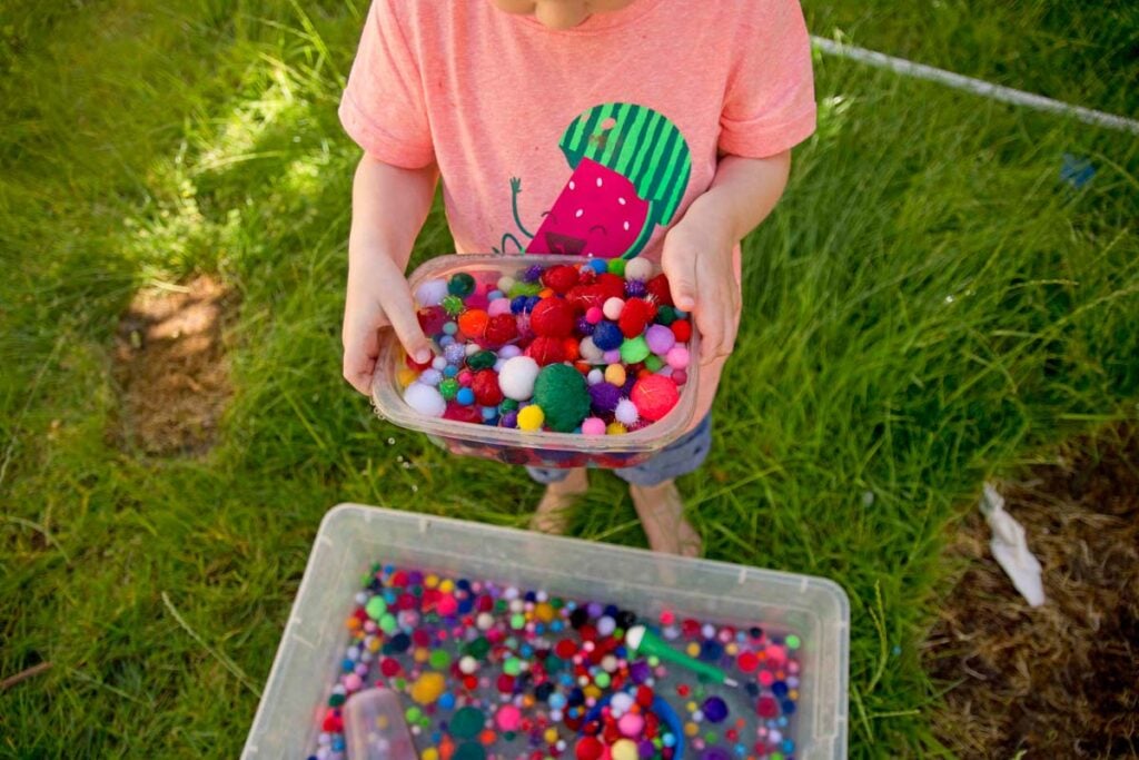 A child holds a container full of wet pom pom balls.